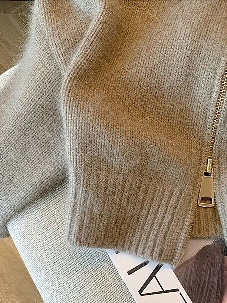 Close-up of a beige knit cardigan with a gold zipper on a neutral background