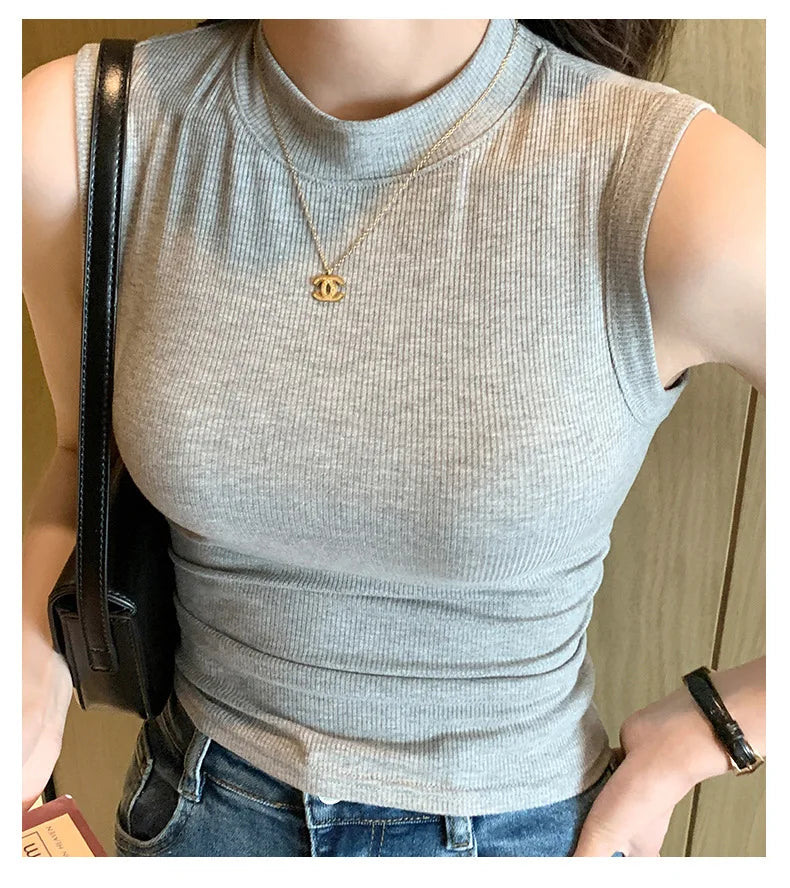 Person wearing a gray sleeveless top with a necklace, holding a black bag.