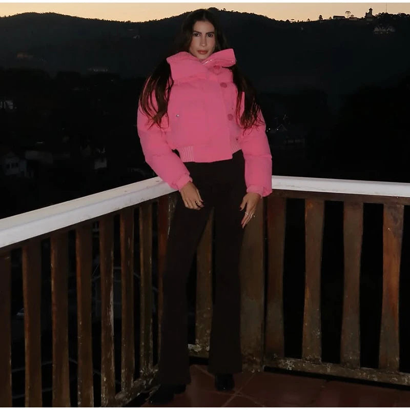Person wearing a pink jacket and black pants standing on a balcony with a dark landscape background