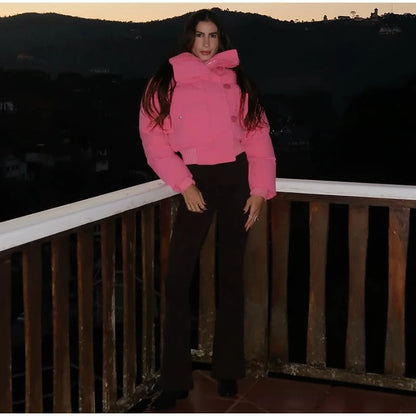 Person wearing a pink jacket and black pants standing on a balcony with a dark landscape background