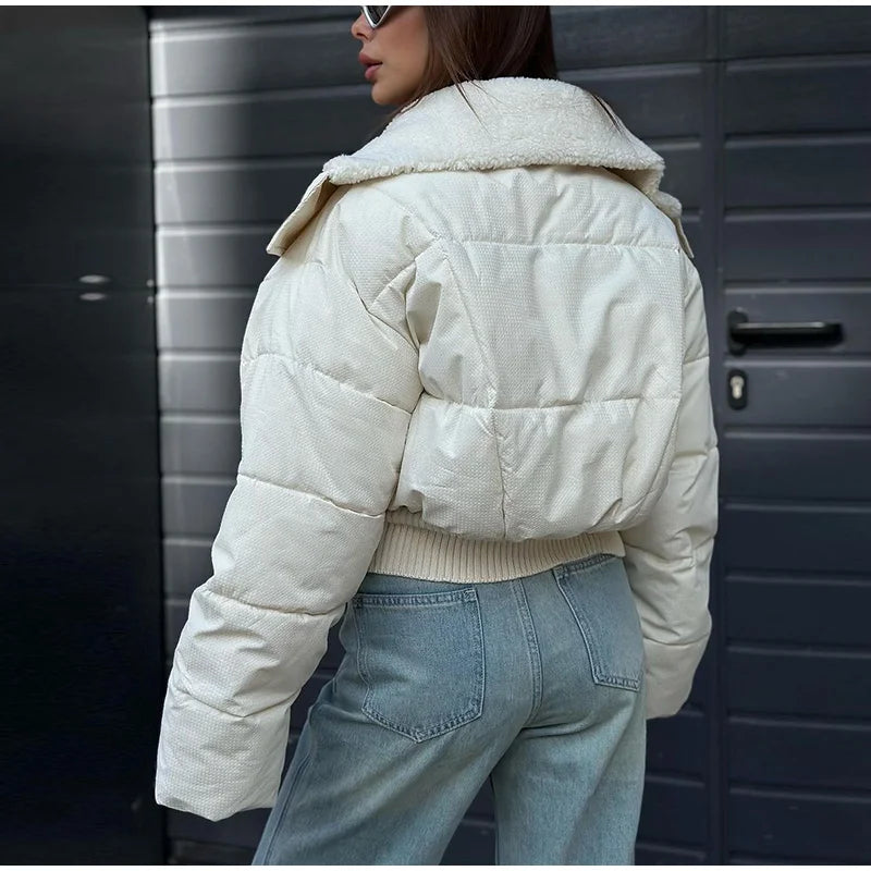Person wearing a white puffer jacket and blue jeans against a dark background