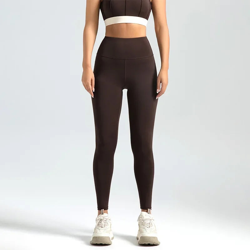 Person wearing brown leggings and a white sports bra on a light gray background