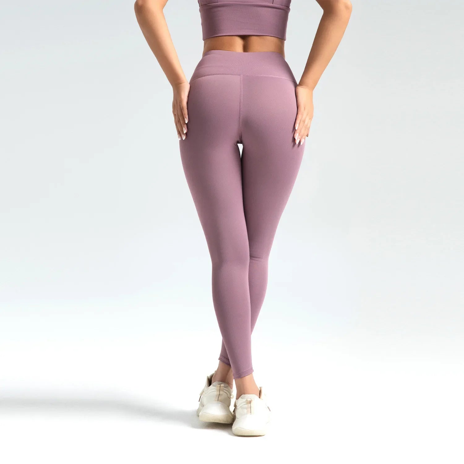 Person wearing mauve leggings and top on a light gray background
