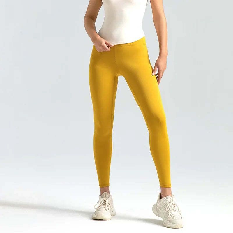 Person wearing mustard yellow leggings with a white top and shoes on a light gray background