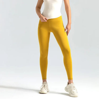 Person wearing mustard yellow leggings with a white top and shoes on a light gray background