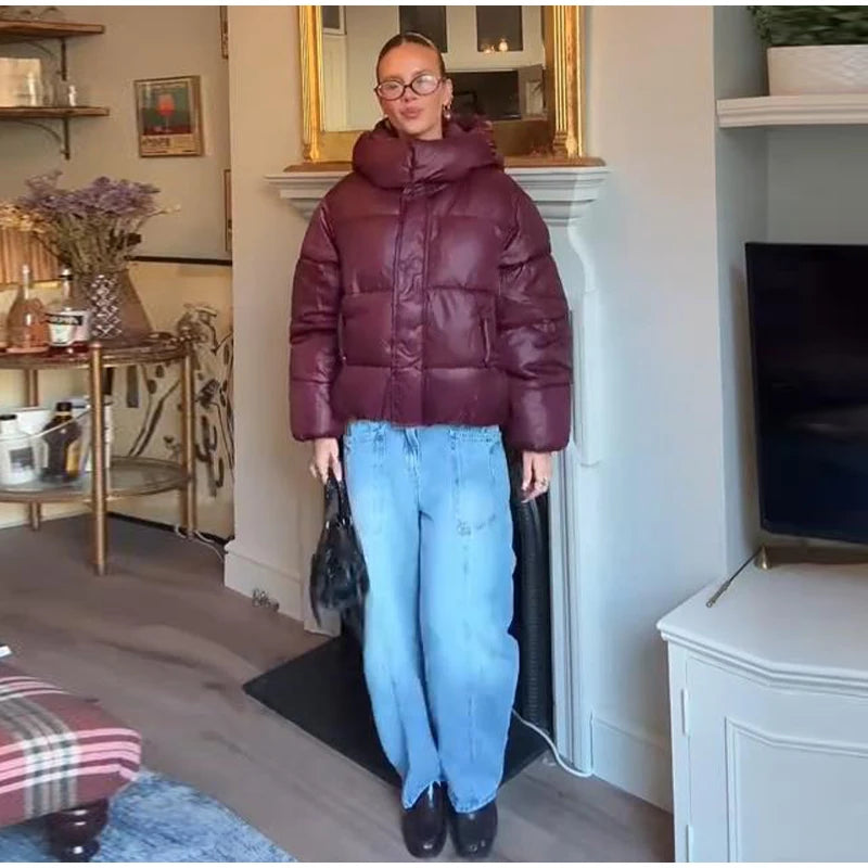 Person wearing a maroon puffer jacket and blue jeans standing in a living room.