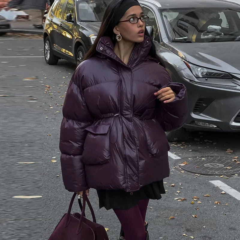 Woman in a purple puffer coat walking on a street with cars in the background
