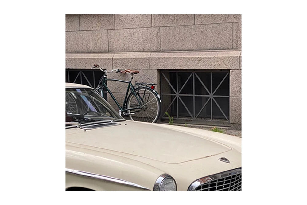 Vintage car with a bicycle leaning against a stone wall.