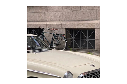 Vintage car with a bicycle leaning against a stone wall.