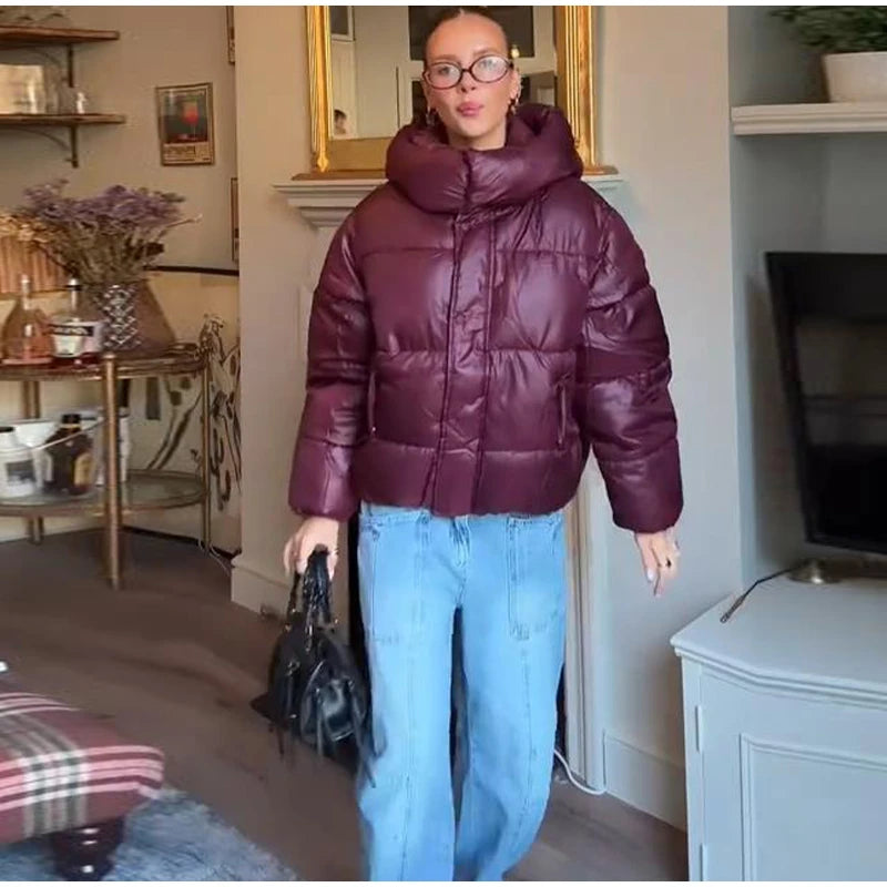 Person wearing a maroon puffer jacket and blue jeans in a living room setting.