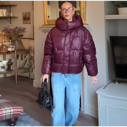 Person wearing a maroon puffer jacket and blue jeans in a living room setting.