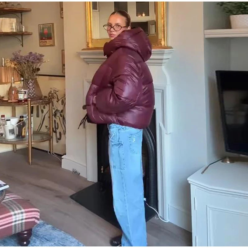 Person wearing a maroon puffer jacket and blue jeans standing in a living room.