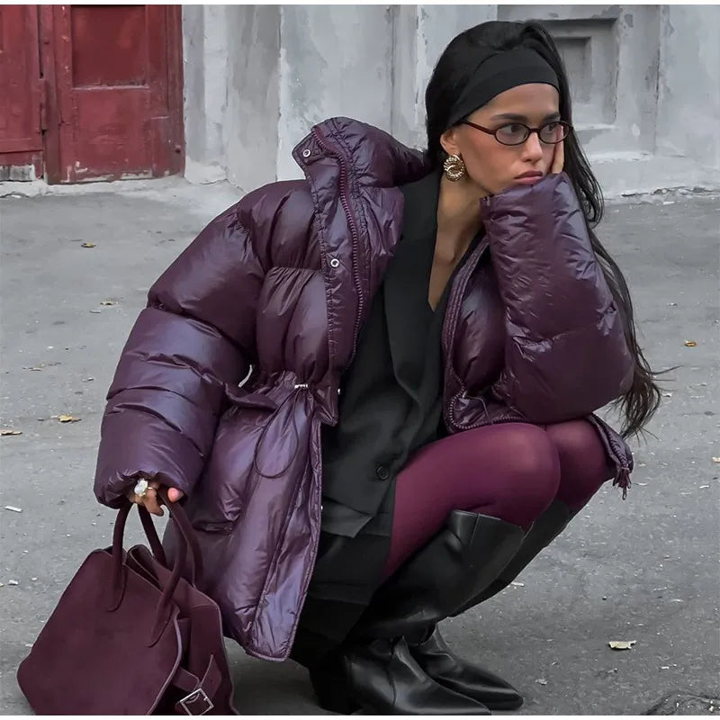 Person wearing a purple puffer coat and holding a matching handbag on a street.