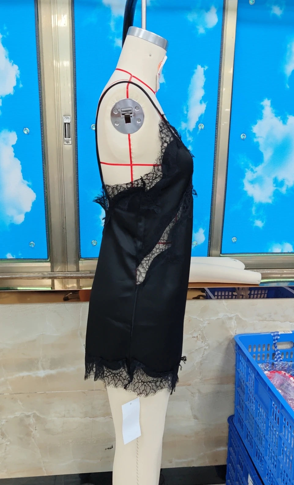 Black lace garment on a mannequin against a blue wall with cloud patterns
