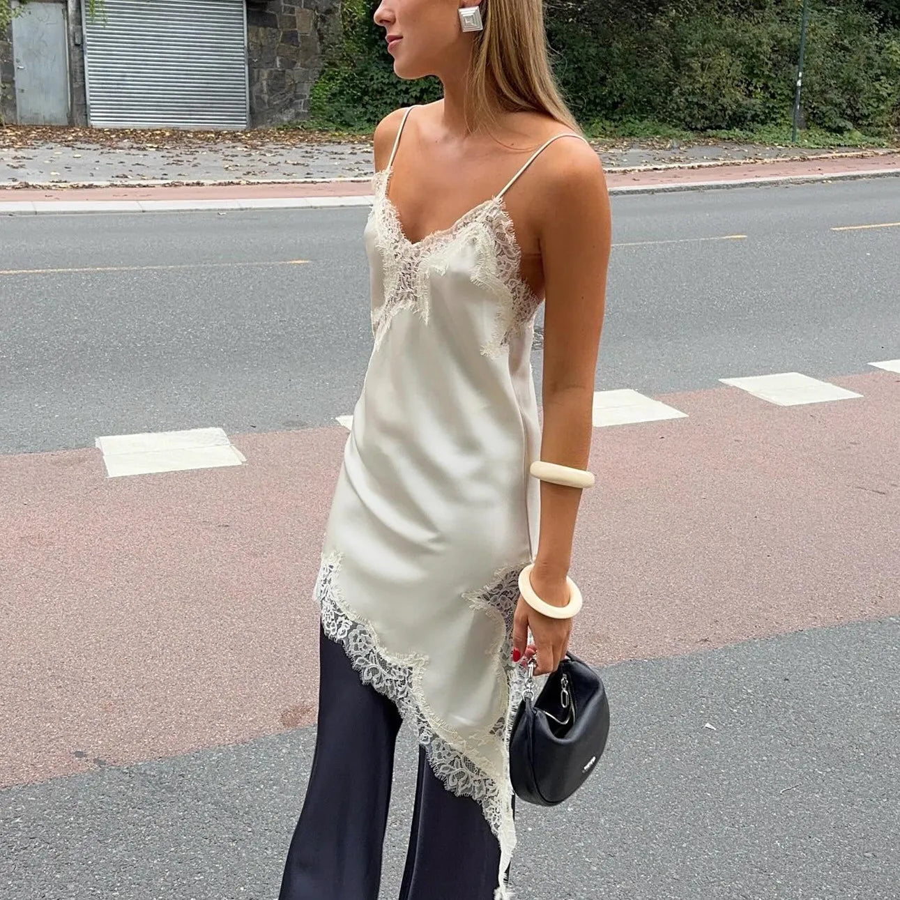 Woman in a white lace top and dark pants walking on a street.