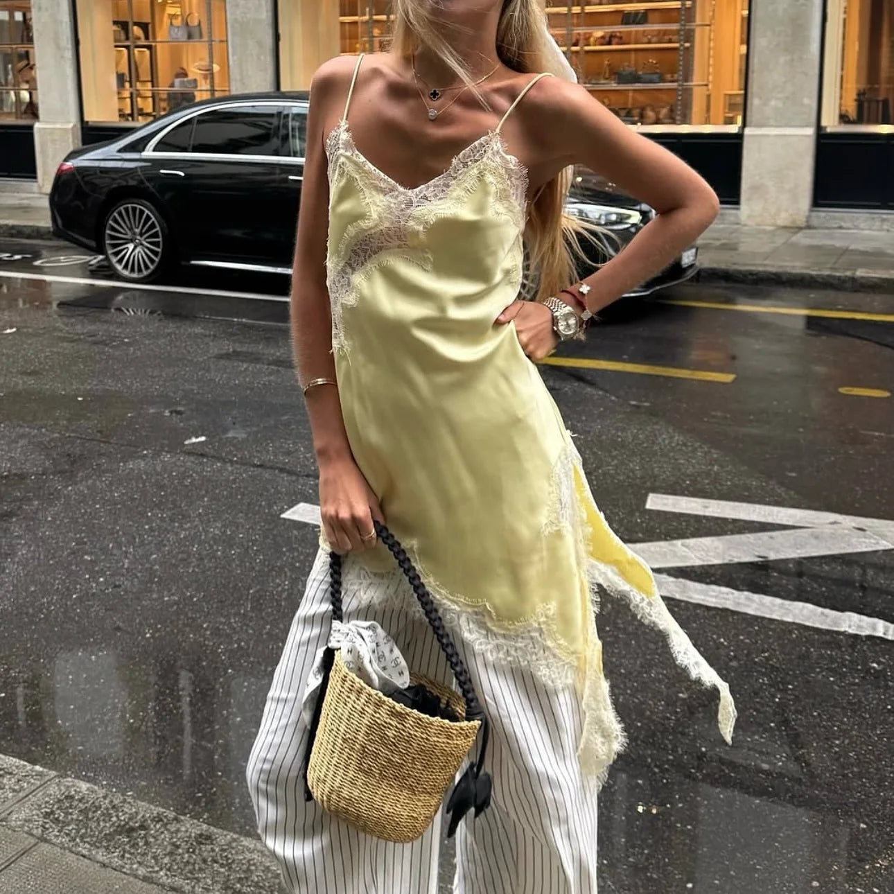 Woman in a yellow slip dress holding a woven bag on a city street.