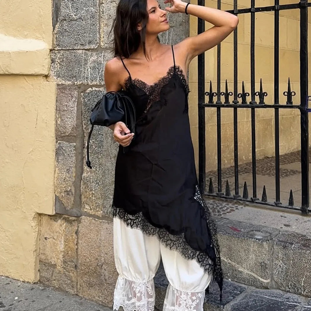 Woman wearing a black lace top and white pants standing against a stone wall.