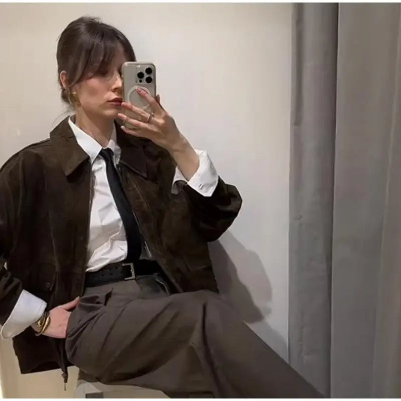 Person taking a mirror selfie wearing a brown jacket and white shirt.