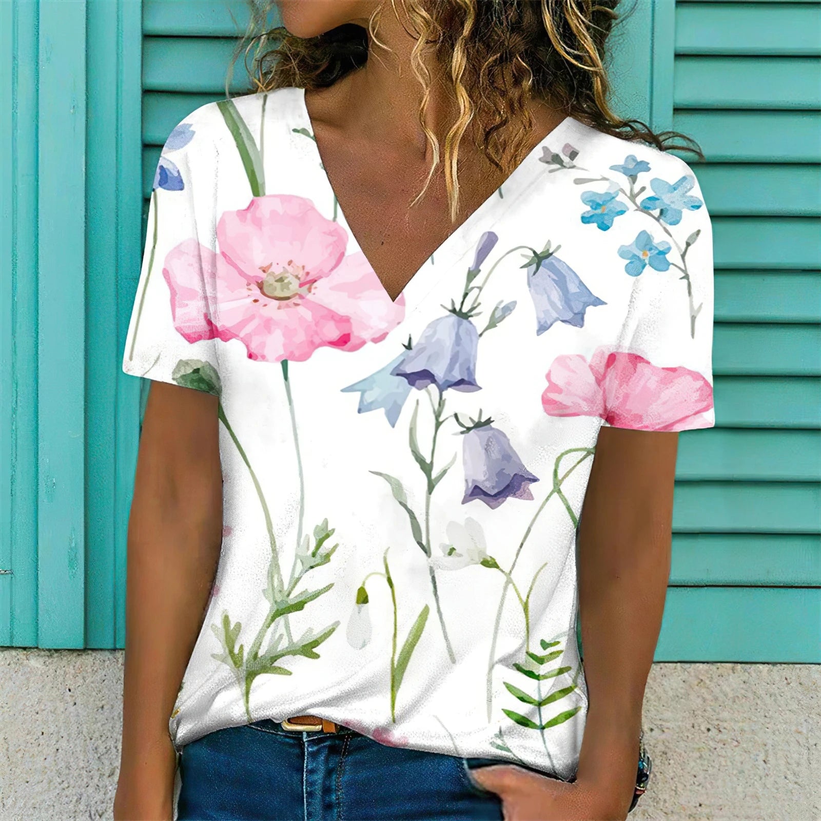 Woman wearing a white V-neck t-shirt with colorful floral designs against a teal background.