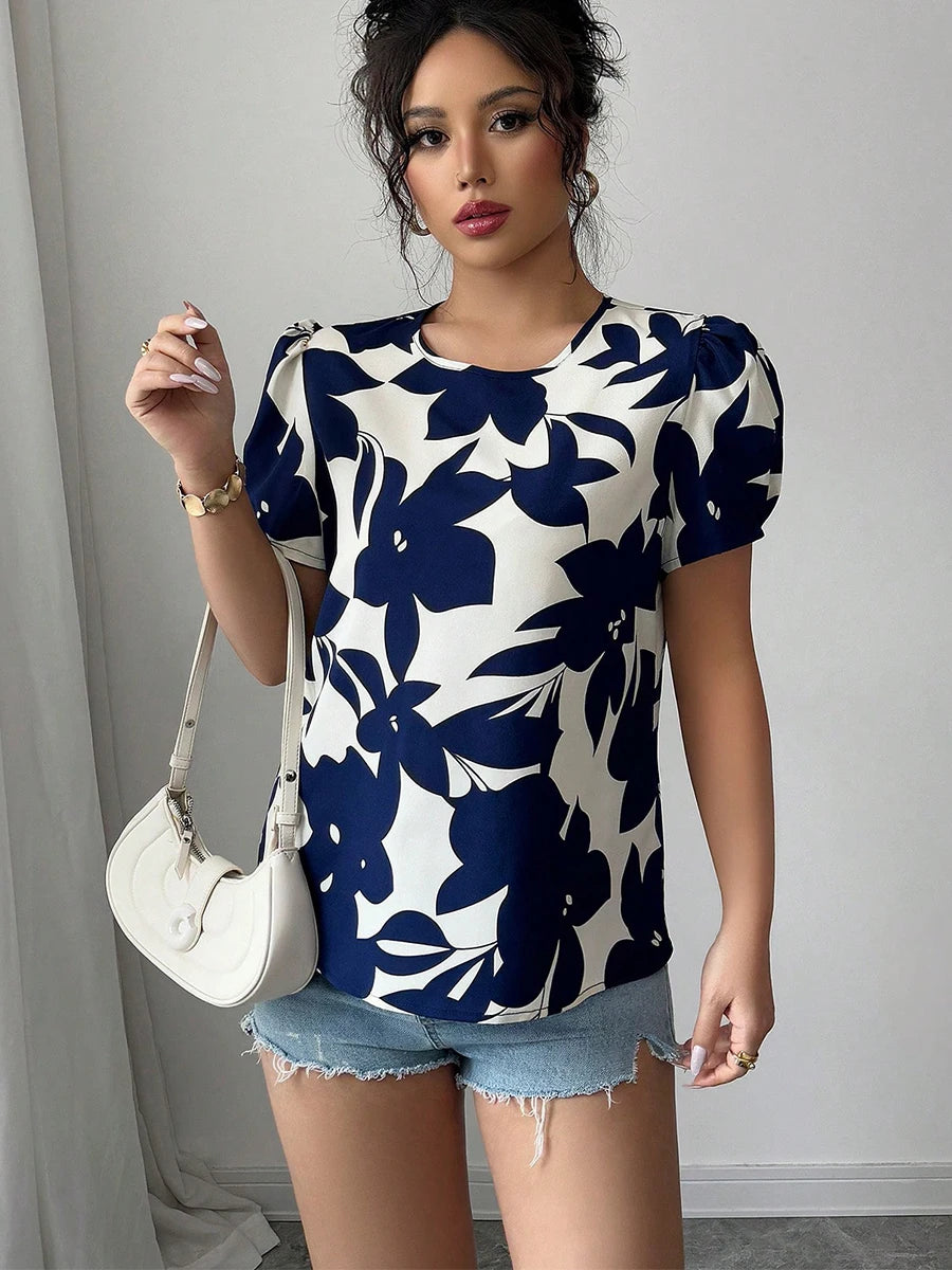 Woman wearing a blue floral patterned shirt with denim shorts, holding a white handbag.