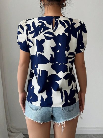 Person wearing a blue and white floral top with denim shorts against a neutral background