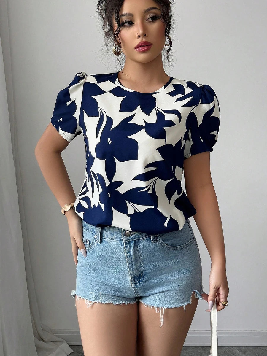 Woman wearing a blue and white floral top with denim shorts against a gray background