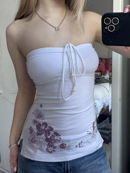 Person wearing a white strapless top with floral patterns, standing in a room.