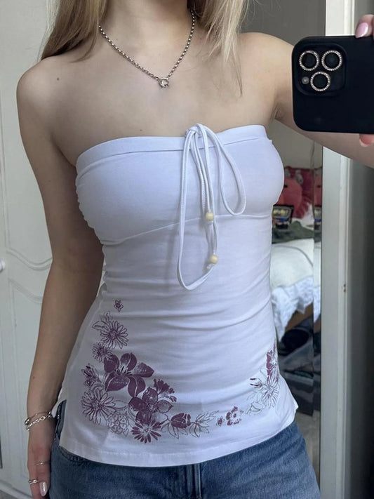Person wearing a white strapless top with floral patterns, standing in a room.