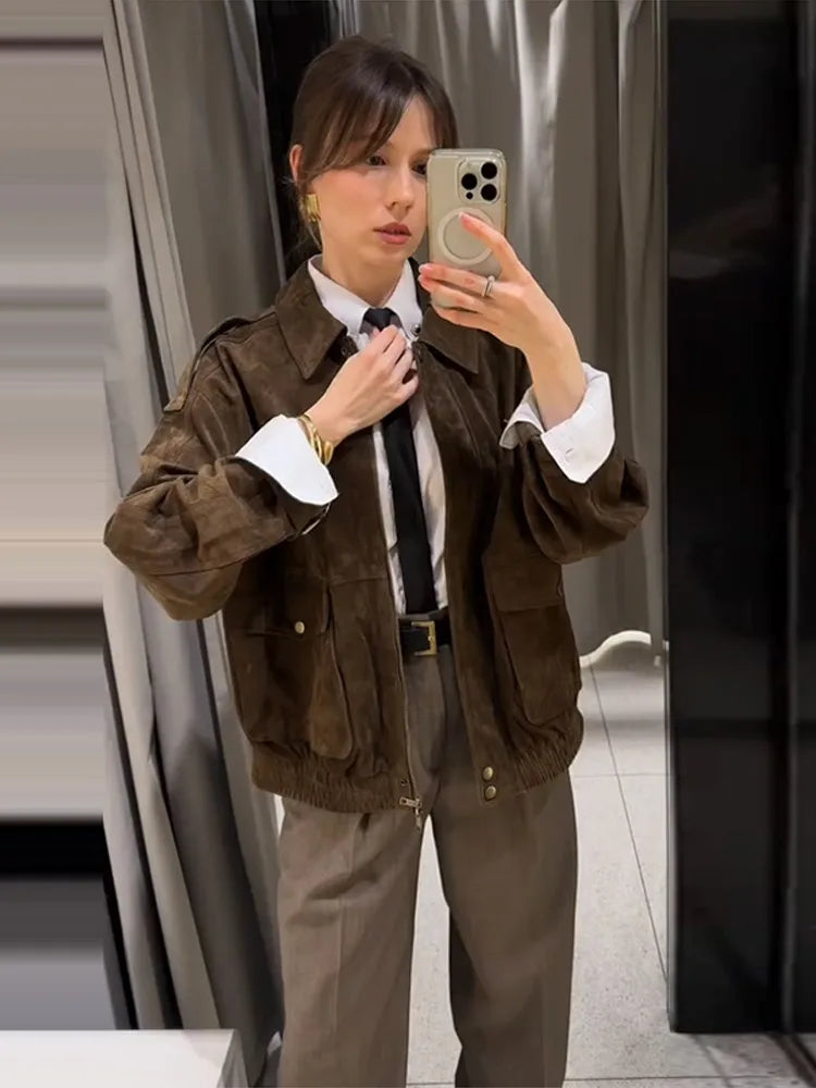 Person taking a mirror selfie wearing a brown jacket and white shirt.