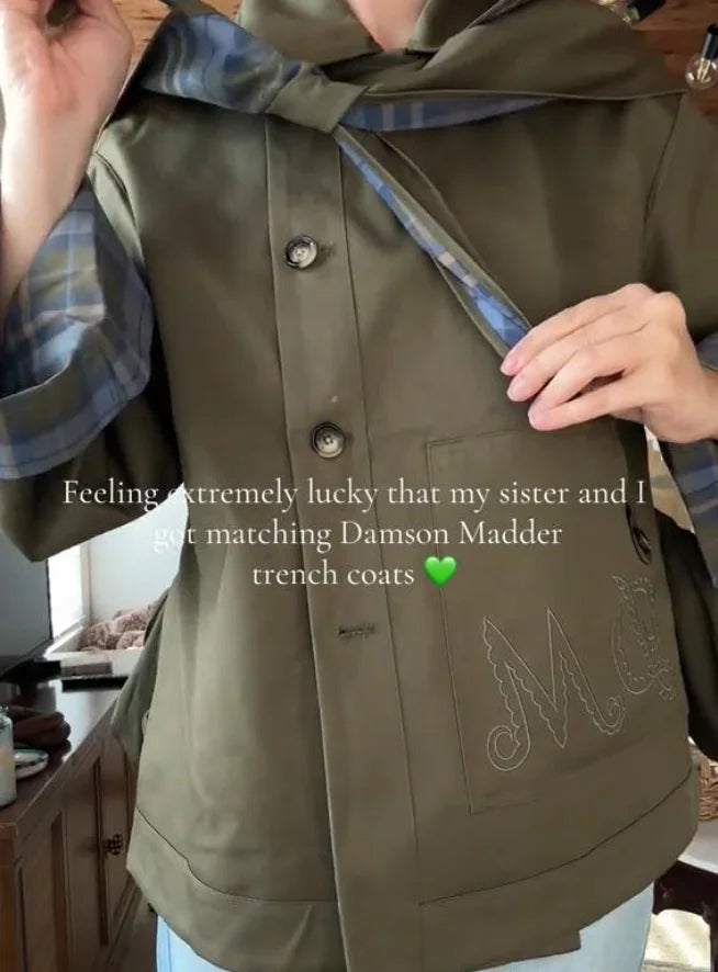 Person wearing a green trench coat with 'ME' embroidery, holding a matching coat.
