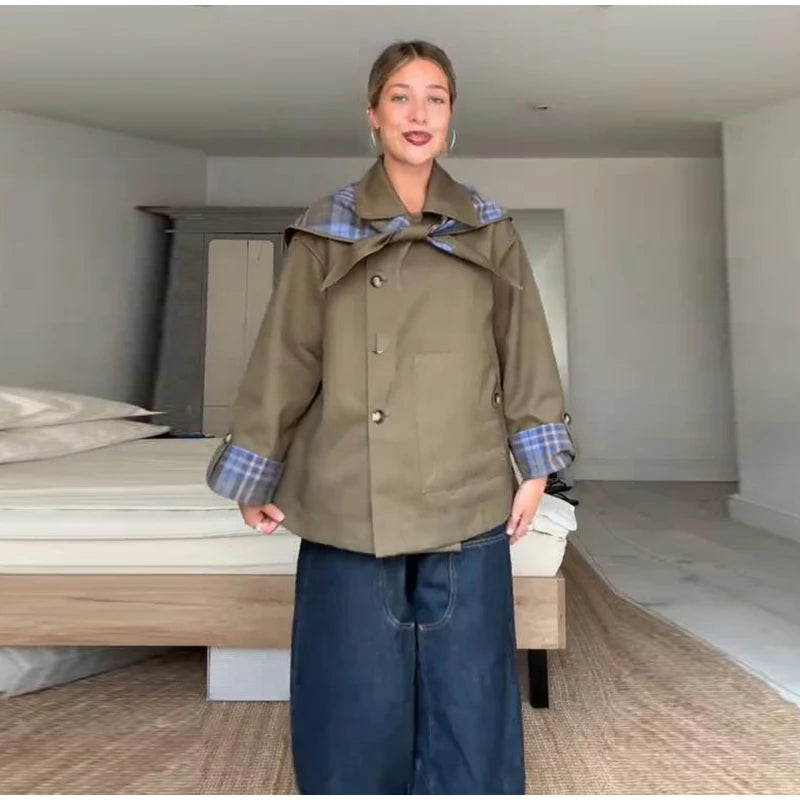 Person wearing a green coat with plaid lining in a minimalistic room.