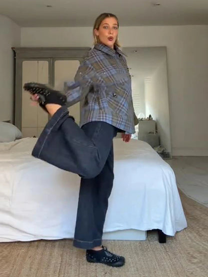 Woman in plaid jacket and jeans posing in a bedroom