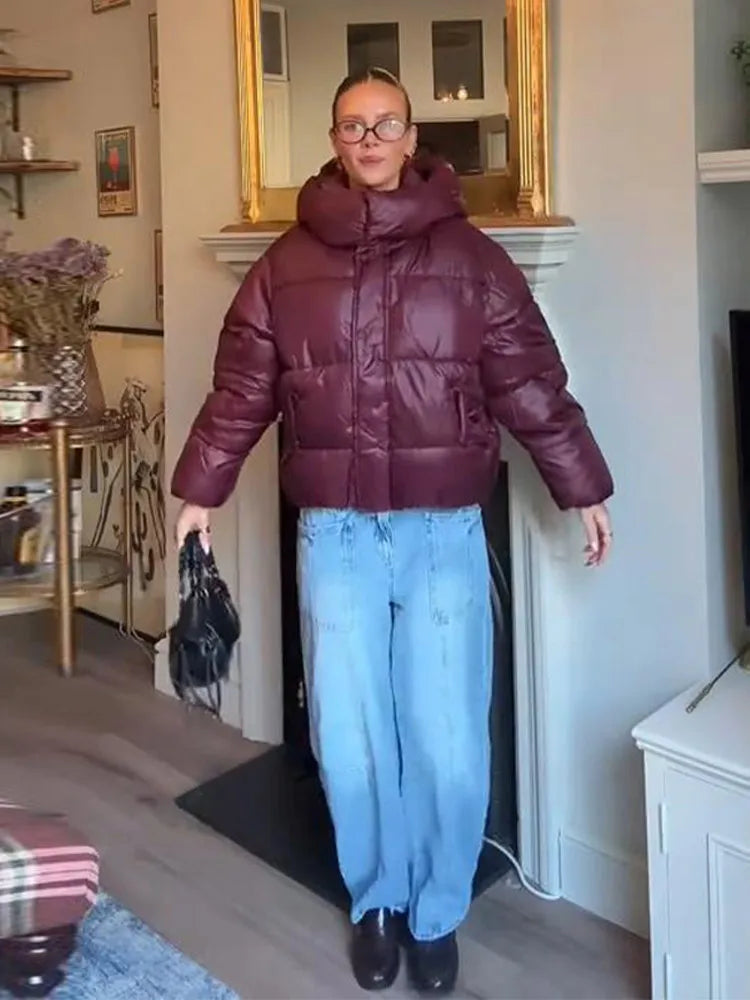 Person wearing a maroon puffer jacket and blue jeans indoors.