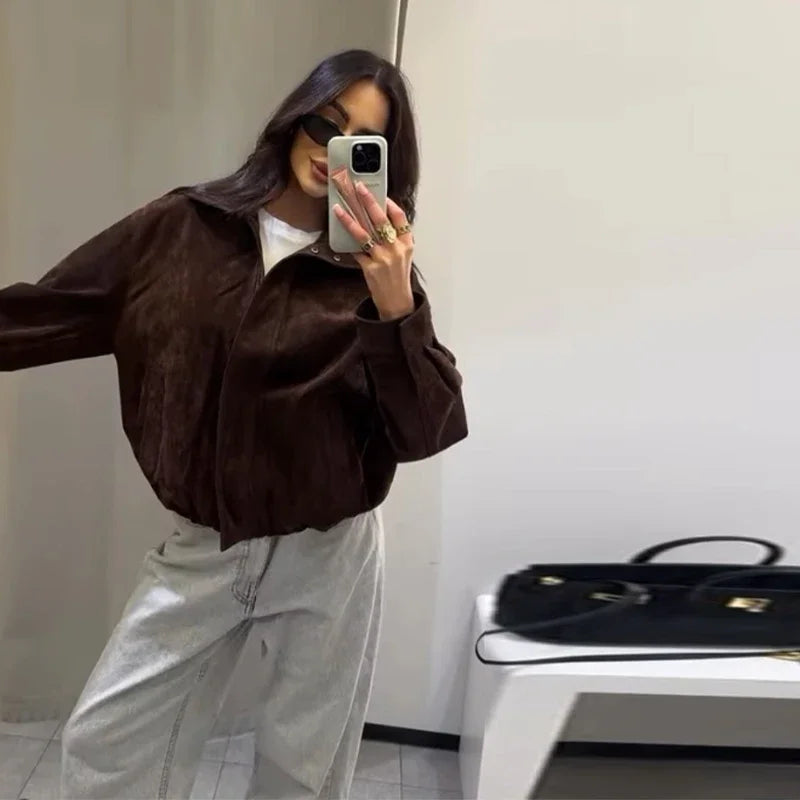 Person wearing a brown jacket and light gray pants taking a mirror selfie.