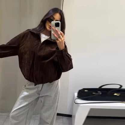 Person wearing a brown jacket and light gray pants taking a mirror selfie.