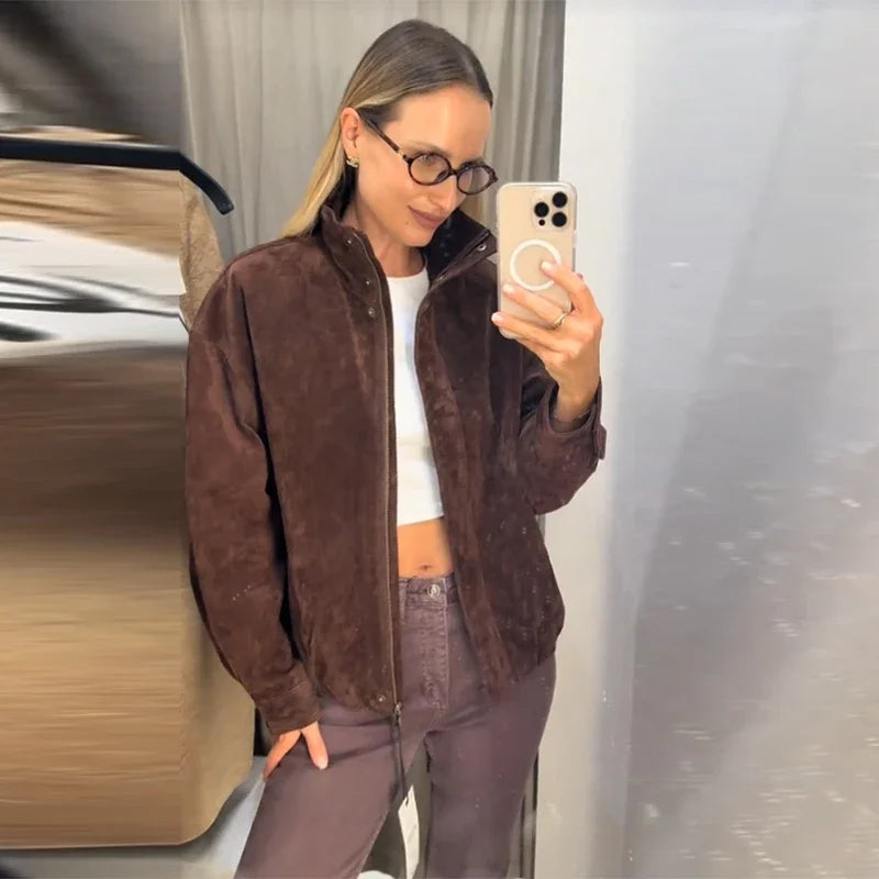 Person taking a mirror selfie wearing a brown jacket and white top.