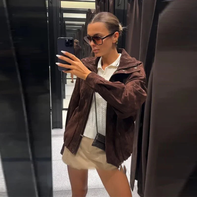 Woman taking a mirror selfie wearing a brown jacket and sunglasses.