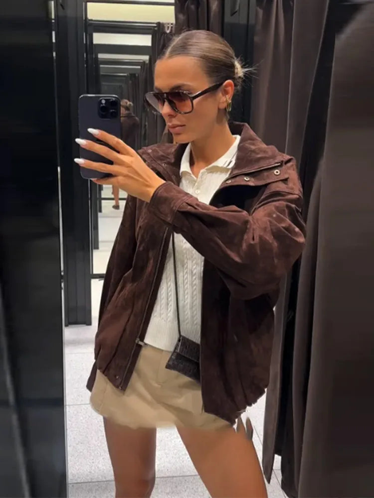 Person taking a mirror selfie wearing a brown jacket and beige shorts.