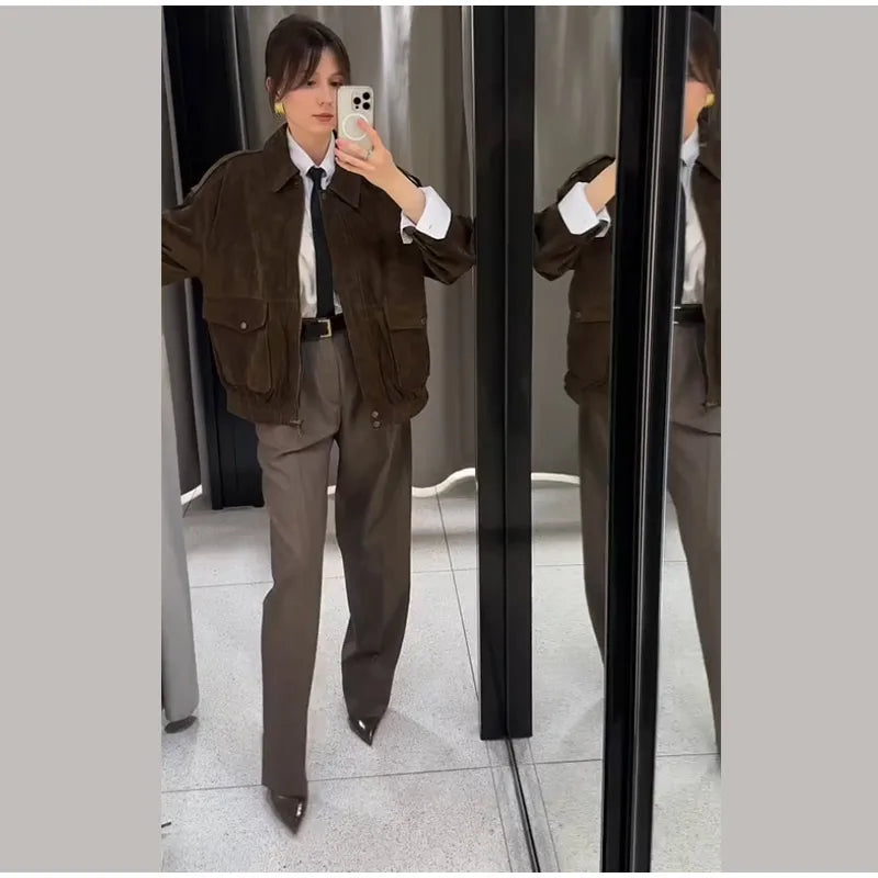Person wearing a brown jacket and gray pants standing in front of a mirror.