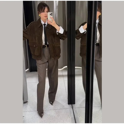Person wearing a brown jacket and gray pants standing in front of a mirror.