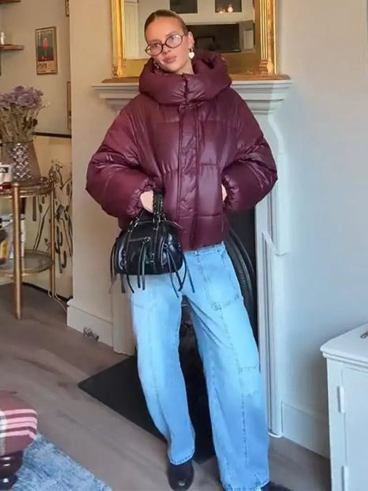 Person wearing a burgundy puffer jacket and light blue jeans indoors.