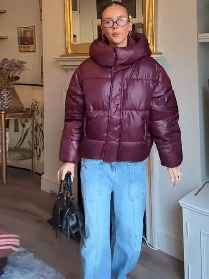Person wearing a maroon puffer jacket and blue jeans indoors.