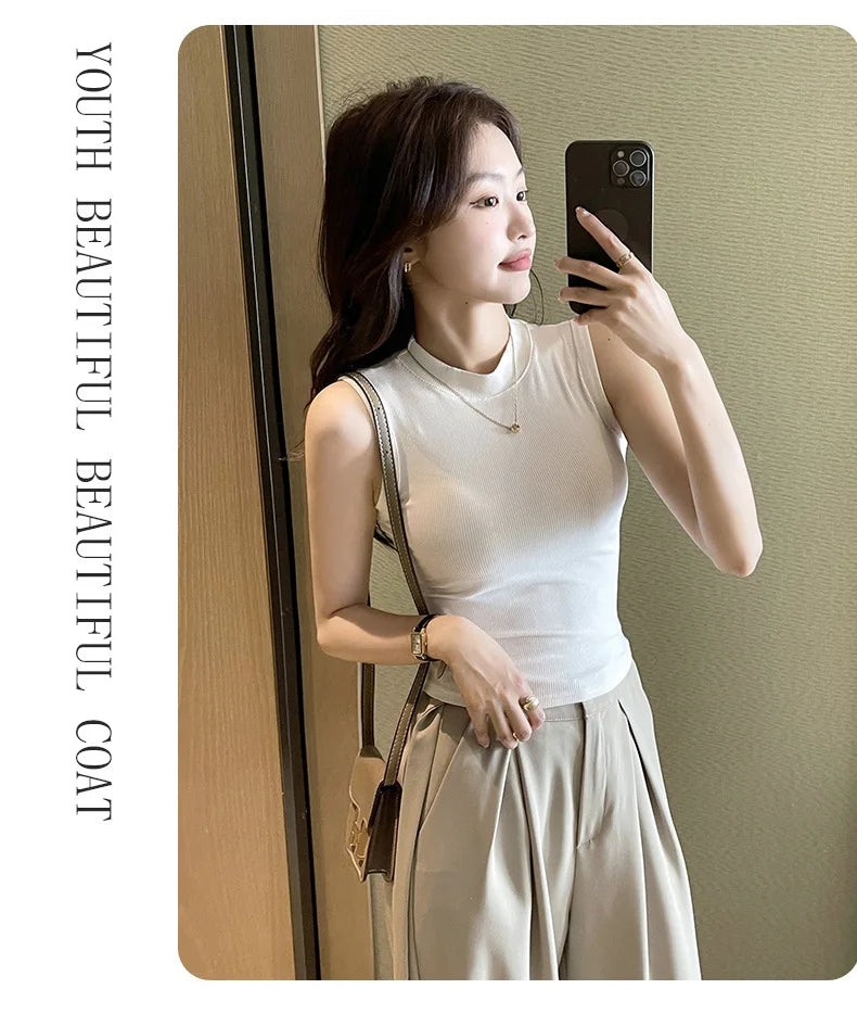 Woman taking a mirror selfie wearing a white sleeveless top and beige pants, with text 'Youth Beautiful Beautiful Coat' on the left.