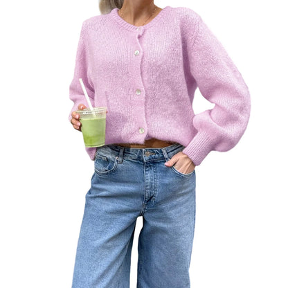 Person wearing a pink cardigan and blue jeans holding a green drink with a straw on a white background