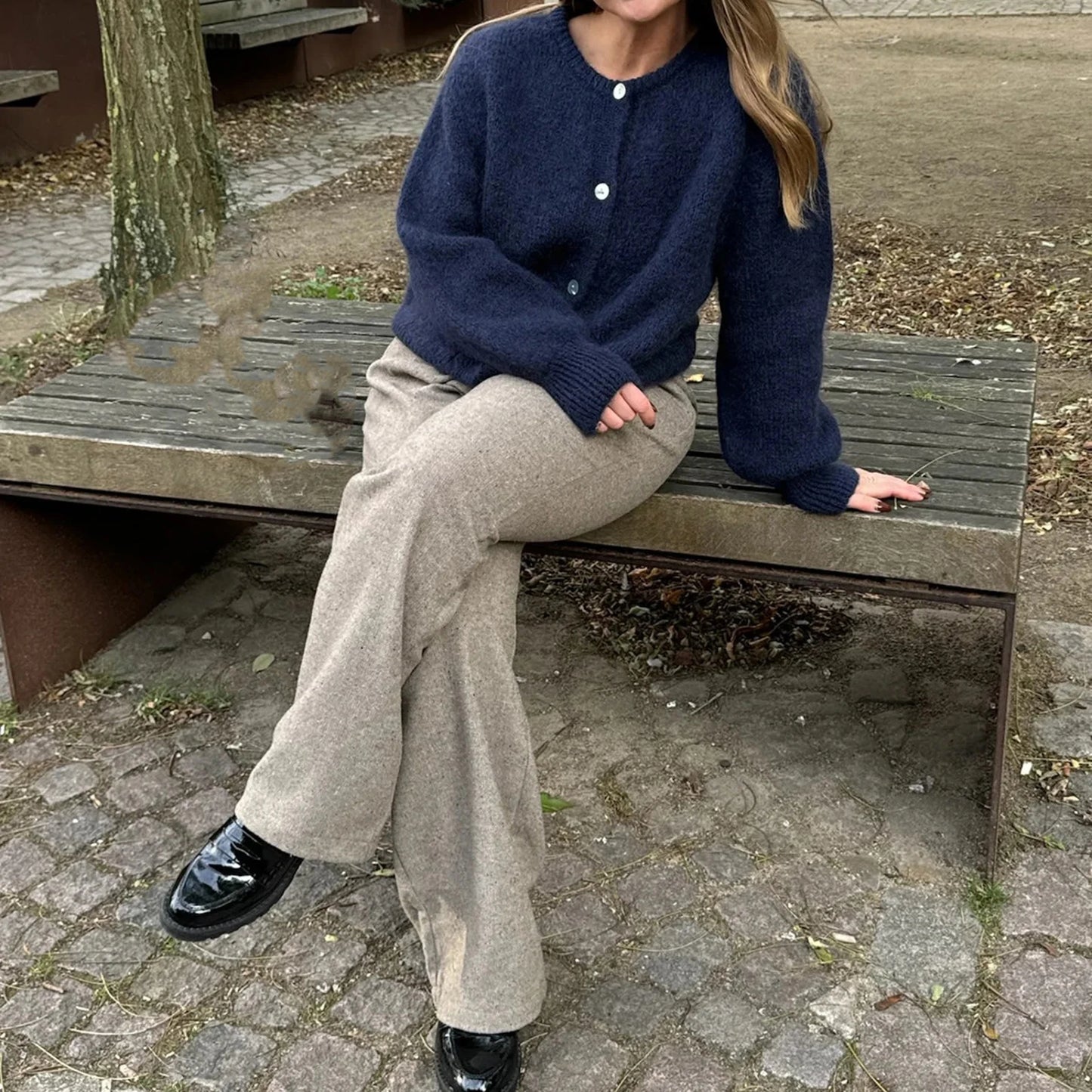 Person sitting on a wooden bench wearing a navy sweater and beige pants.