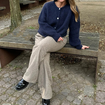 Person sitting on a wooden bench wearing a navy sweater and beige pants.