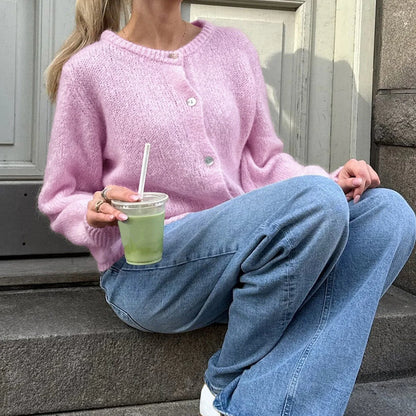 Person wearing a pink sweater and blue jeans, sitting on steps holding a drink.