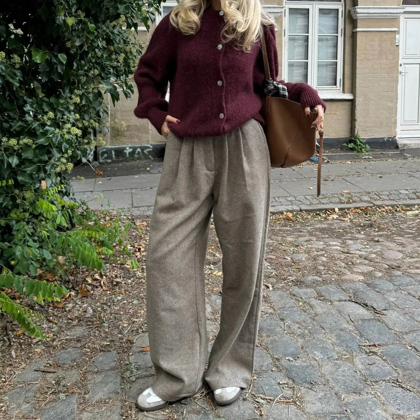 Person wearing a burgundy cardigan and beige pants standing on a cobblestone street.