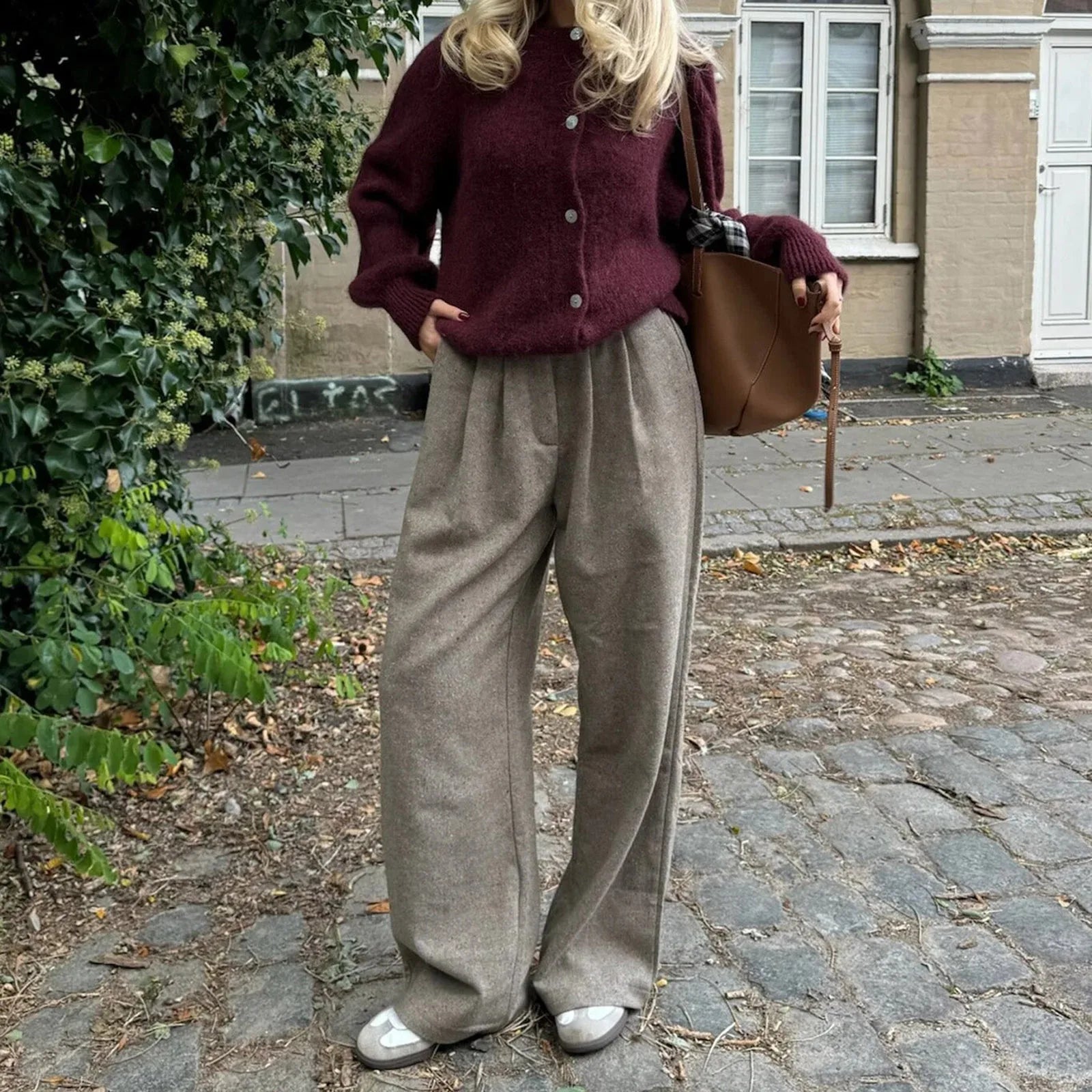 Person wearing a burgundy cardigan and beige pants standing on a cobblestone street.