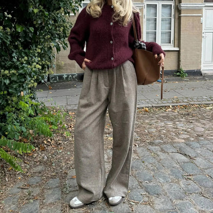 Person wearing a burgundy cardigan and beige pants standing on a cobblestone street.